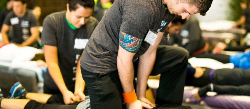 A man pressing his fists against the back of a person lying on a mat on the floor during a Sports Massage event at NHI Massage School